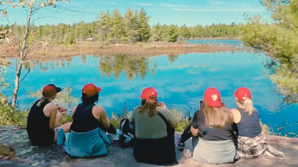 Five women in red caps sitting together overlooking a lake in Canada.